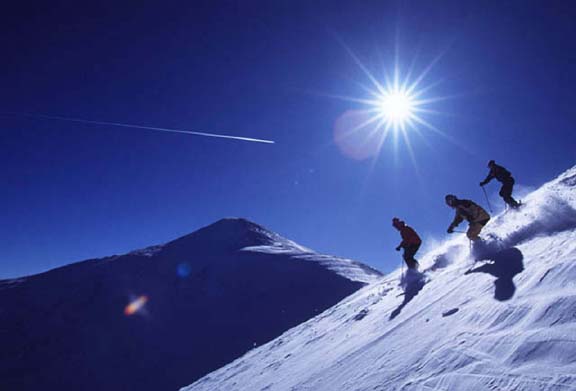 photos of skiers on white slope, with dark blue sky and white Sun